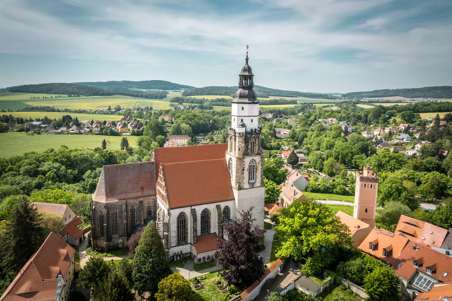 St. Marienkirche mit hohem Turm und Roter Turm mit quadratischem Grundriss in Kamenz, umgeben von roten Dächern und grüner Landschaft / St. Marienkirche with tall tower and Roter Turm with square base in Kamenz, surrounded by red roofs and green landscape