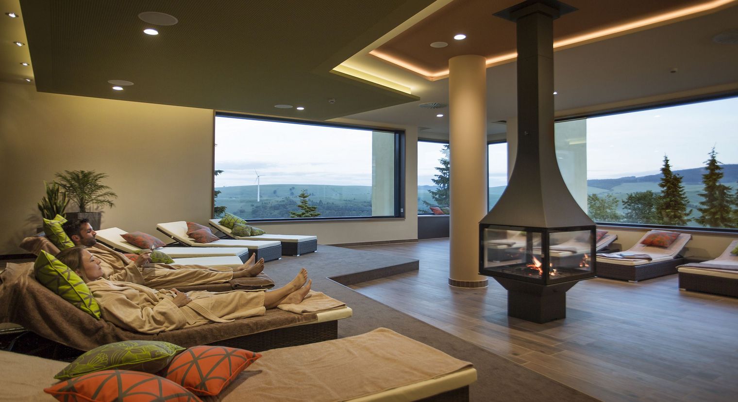 Ein Mann und eine Frau liegen auf einer der Liegen im Elldus Resort Oberwiesenthal. Im Hintergrund kann man die Landschaft vom Erzgebirge sehen.