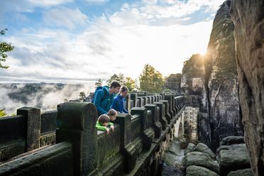 Menschen schauen von der Basteibrücke in der Sächsischen Schweiz herunter in die Landschaft. 