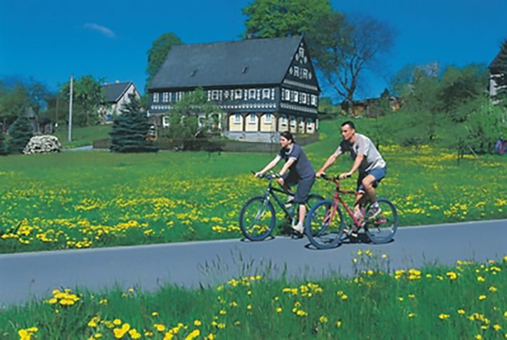 Zwei Radfahrer in der Oberlausitz, im Hintrgrund ein Umgebindehaus