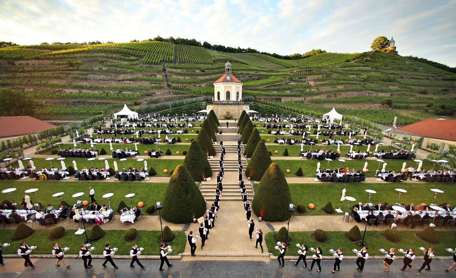 Besucher sitzen auf dem Anwesen Schloss Wackerbarth und werden von den Kellnern bedient. Es ist Sommernachtsball. 