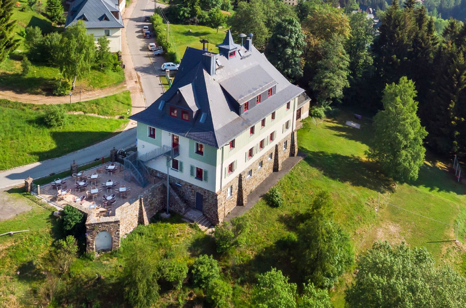 Die Jugendherberge Johanngeorgenstadt von oben fotografiert. Rundherum sind Wiesen, Wälder und einzelne Häuser.