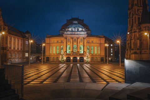 Beleuchtetes Opernhaus Chemnitz bei Nacht mit zwei Weihnachtsbäumen auf dem Platz davor. / Illuminated Chemnitz Opera House at night with two Christmas trees on the square in front.